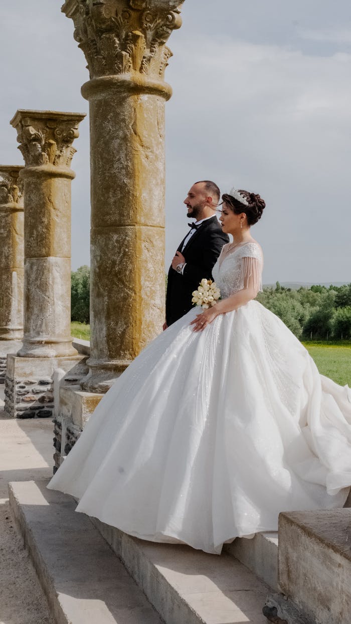 A bride and groom stand together in wedding attire by colonnades, capturing timeless romance.
